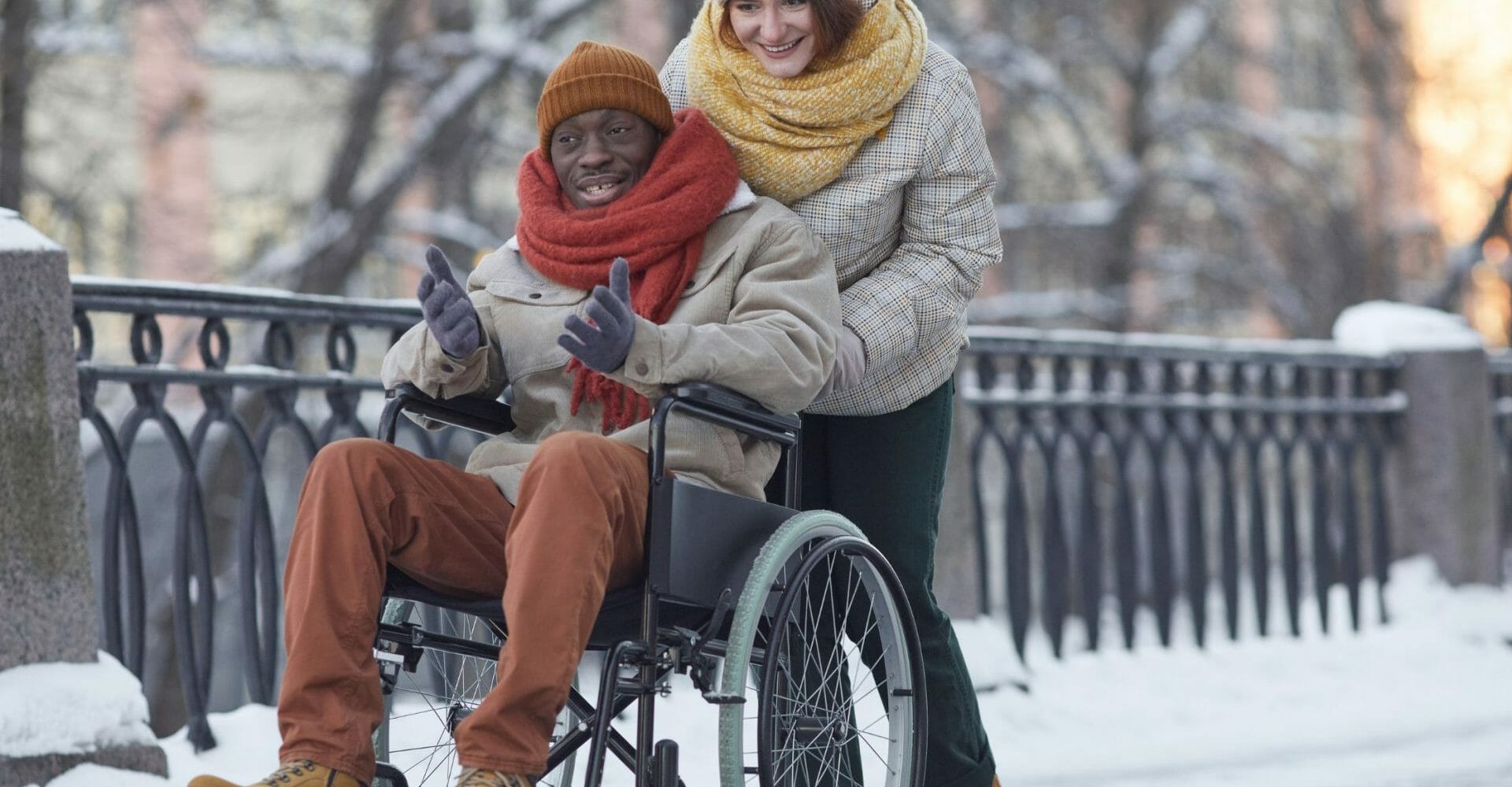 homme en fauteuil roulant avec une accompagnatrice, à l'extérieur en hiver.